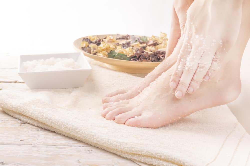womans feet with sugar scrub on them with sugar and herbs in the background