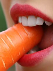 close up image of womans mouth and teeth eating raw carrot