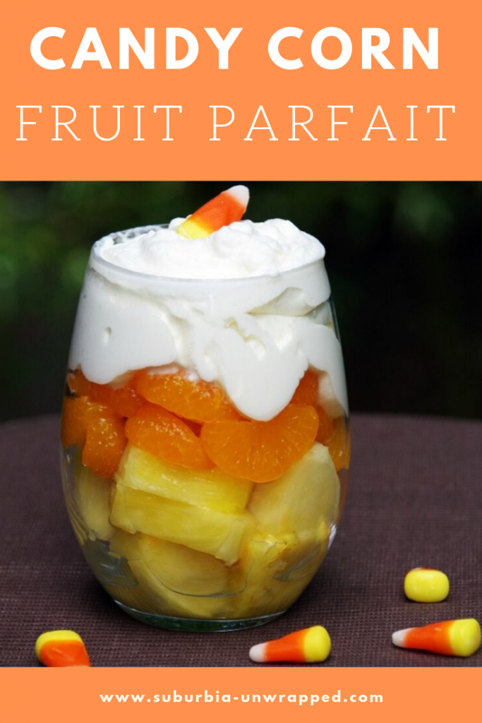 Layers of pineapple and orange slices in a parfait glass topped with whipped cream and candy corn for a healthy Halloween dessert