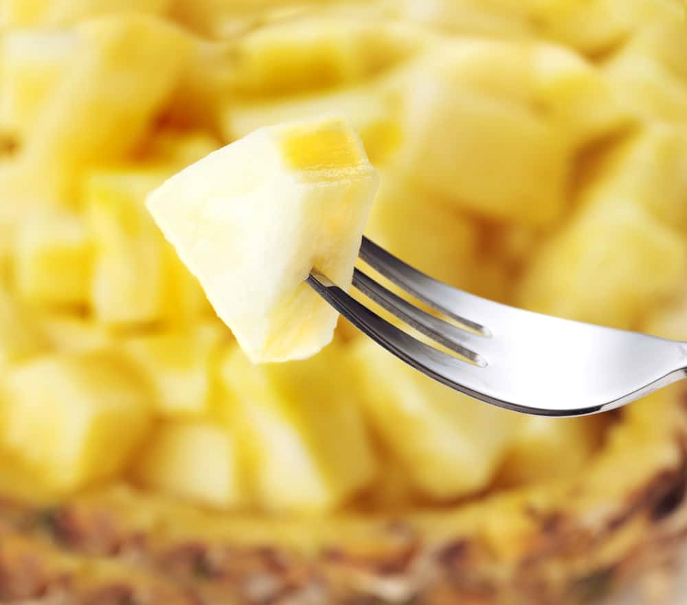 bowl of fresh pineapple with fork holding one piece