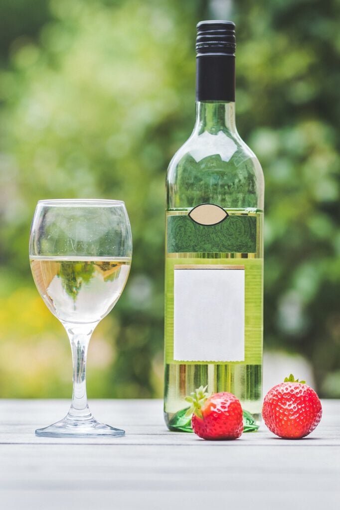 bottle of white wine and glass of wine with strawberries on table