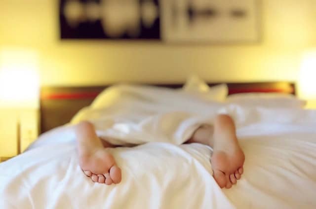 person sleeping in bed with feet hanging out of covers