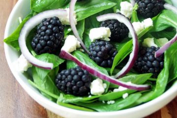 spinach and basil salad with onions and feta in a white bowl