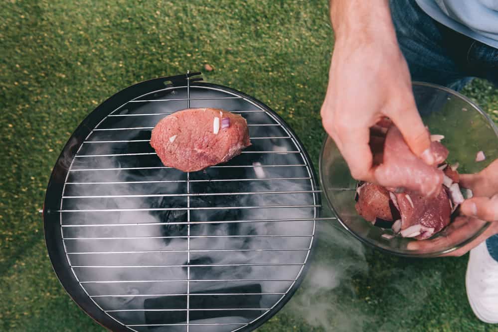 man cooking raw meat on grill