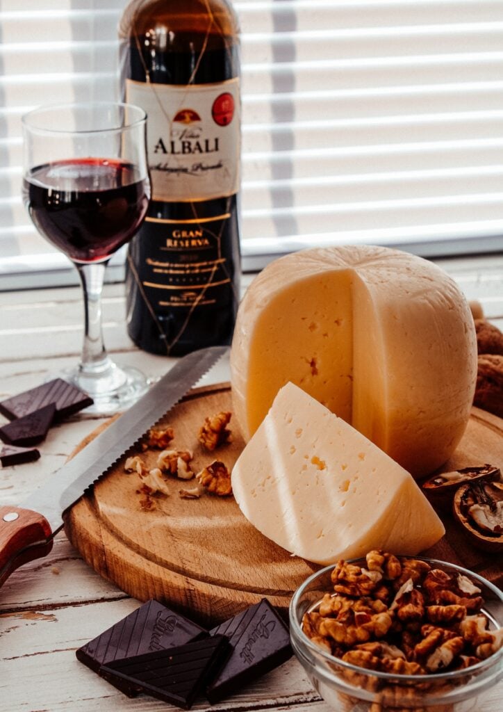 cheese on a cutting board with nuts and red wine in the background