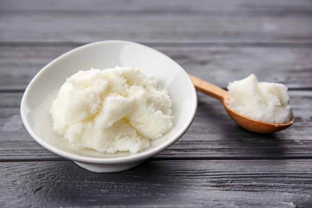 Shea butter in spoon and bowl on wooden background