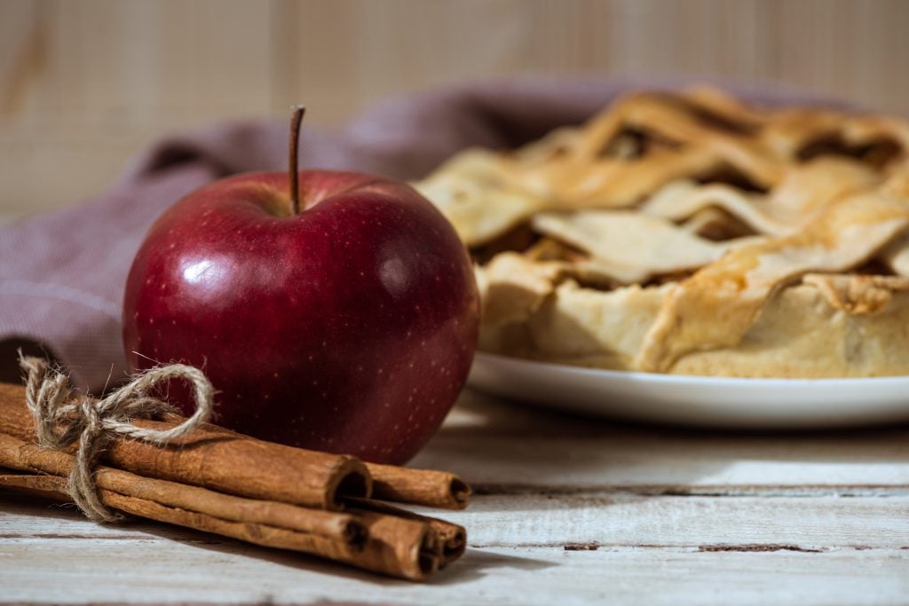 apple and cinnamon sticks in front of a pie on a wood table