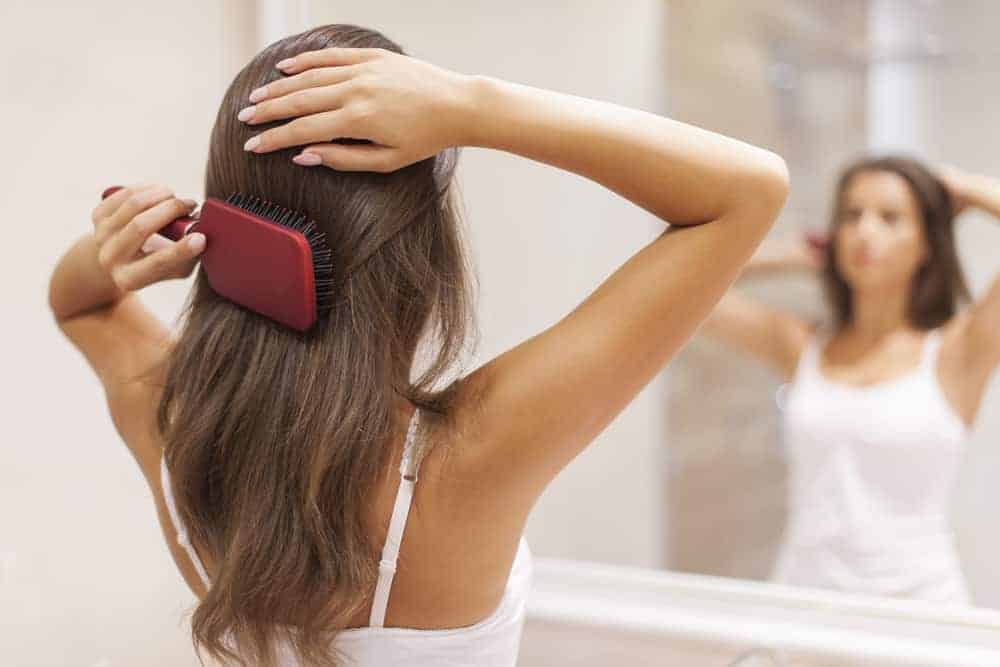 Young woman brushing healthy hair in front of a mirror to reference positive body image in girls