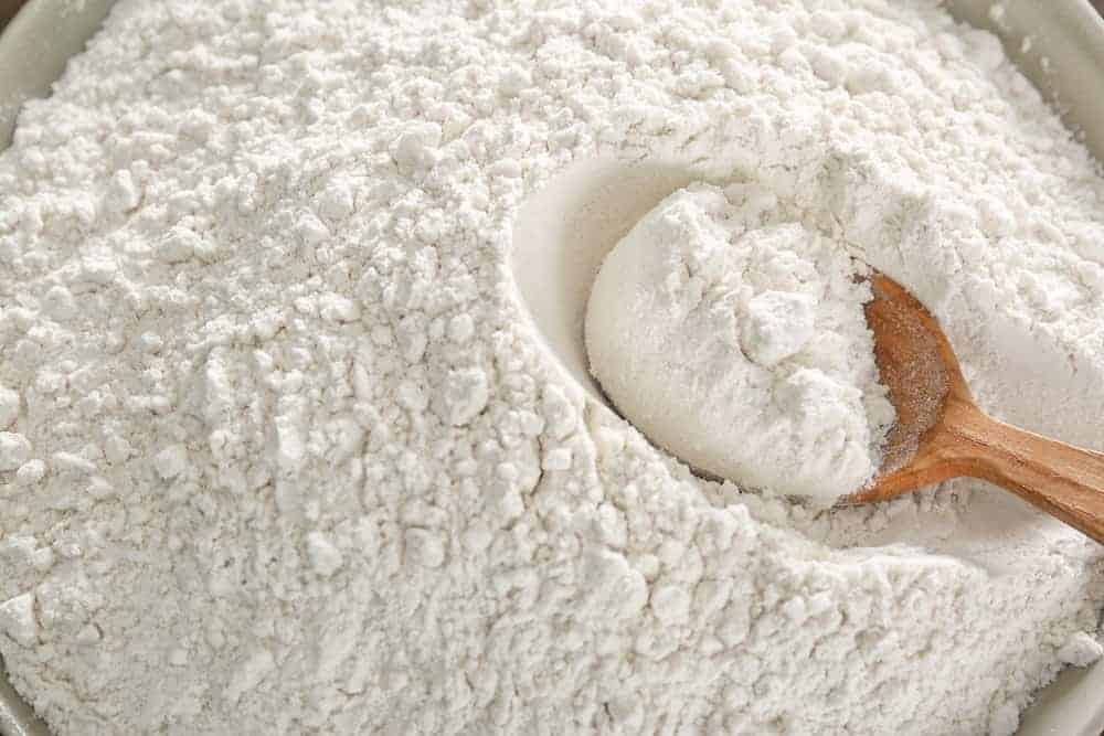 Wheat flour and wooden spoon in bowl, closeup