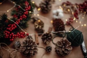 Pine cones, fir branches, wreath, red berries, thread, scissors, cinnamon, cotton, lights on rustic wooden background. Details for making christmas wreath at workshop. Atmospheric image