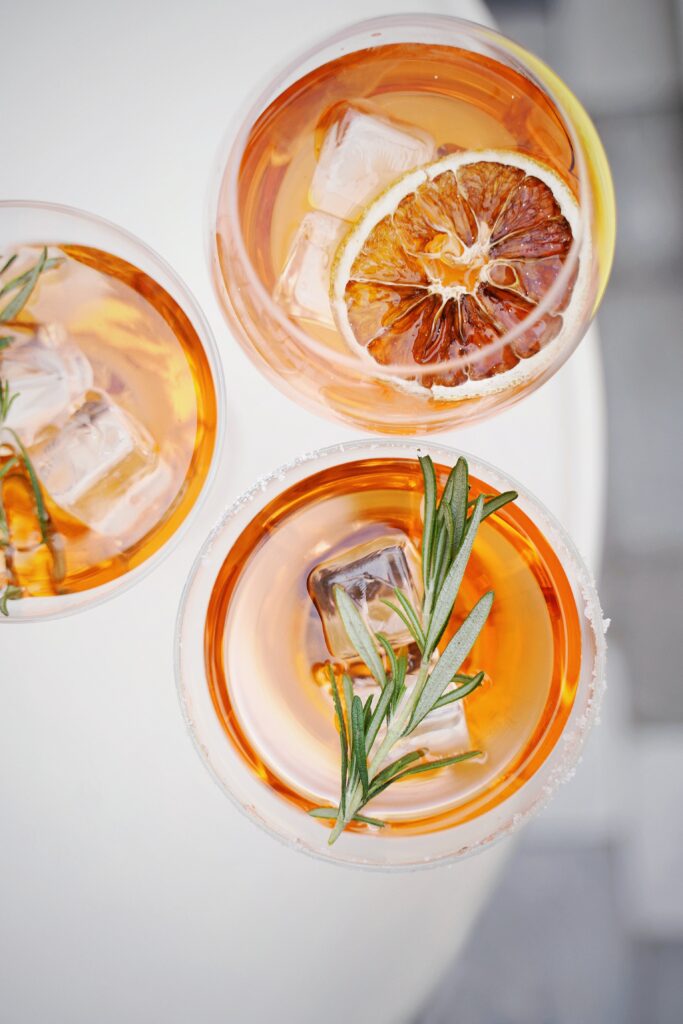 sliced oranges and fresh herbs in several cocktail glasses with orange cocktails