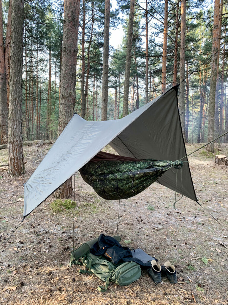 hammock in woods with tarp over it and accessories in pile underneath