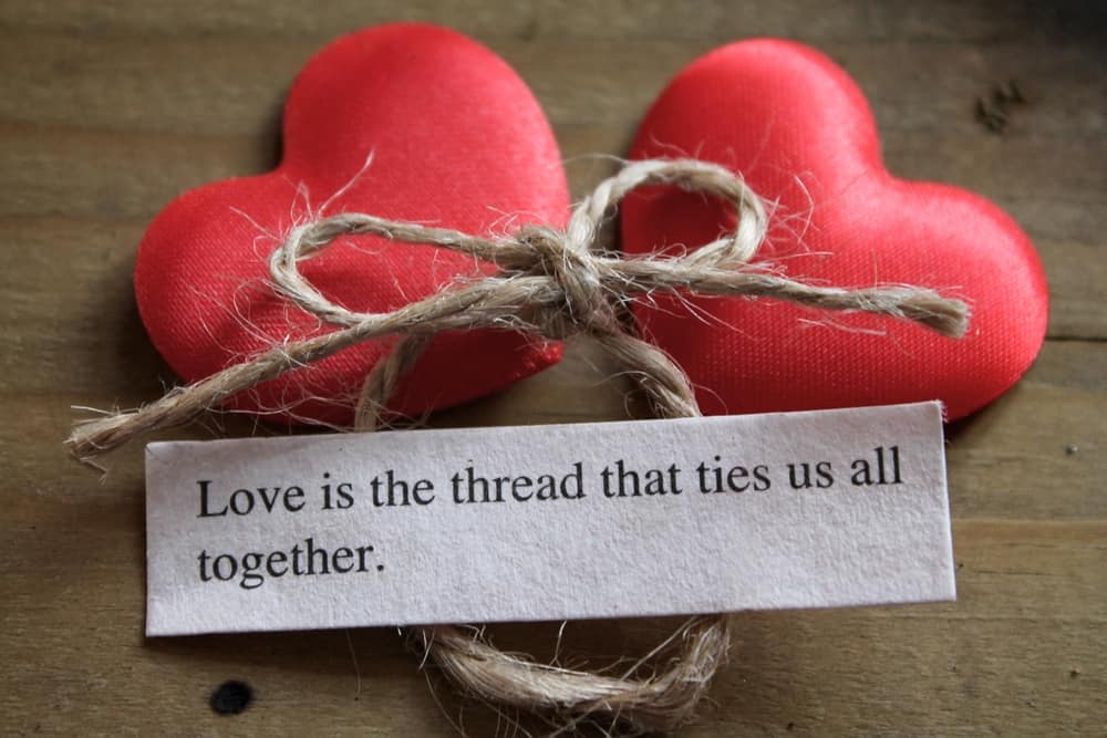 two hearts with string and paper that says love is the thread that ties us all together