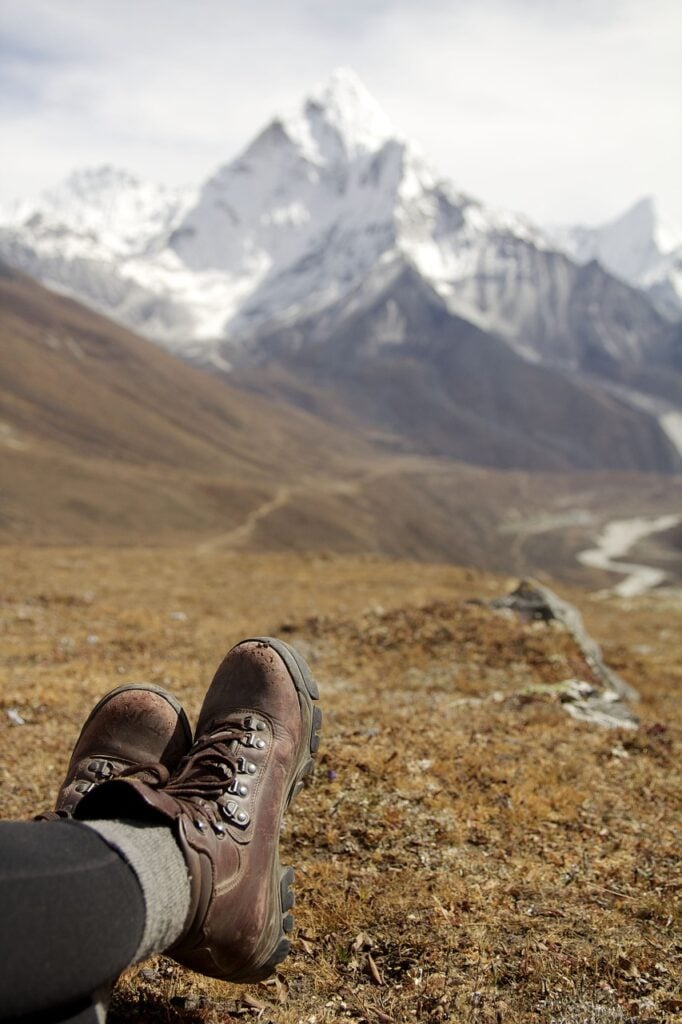 close up of hiking boots on open grassy area with mountains in background