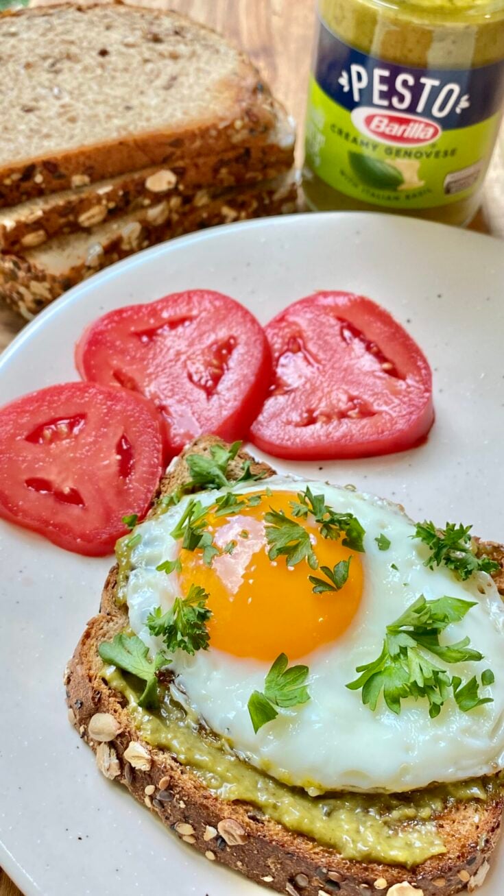 egg pesto toast on plate with fresh tomato slices and jar of barilla pesto sauce in background