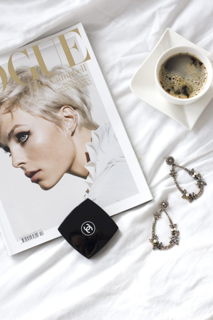 magazine on a white bed with jewelry and coffee