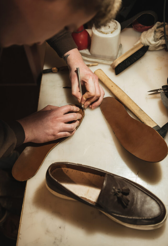Cropped image of young concentrated man shoemaker at footwear workshop.