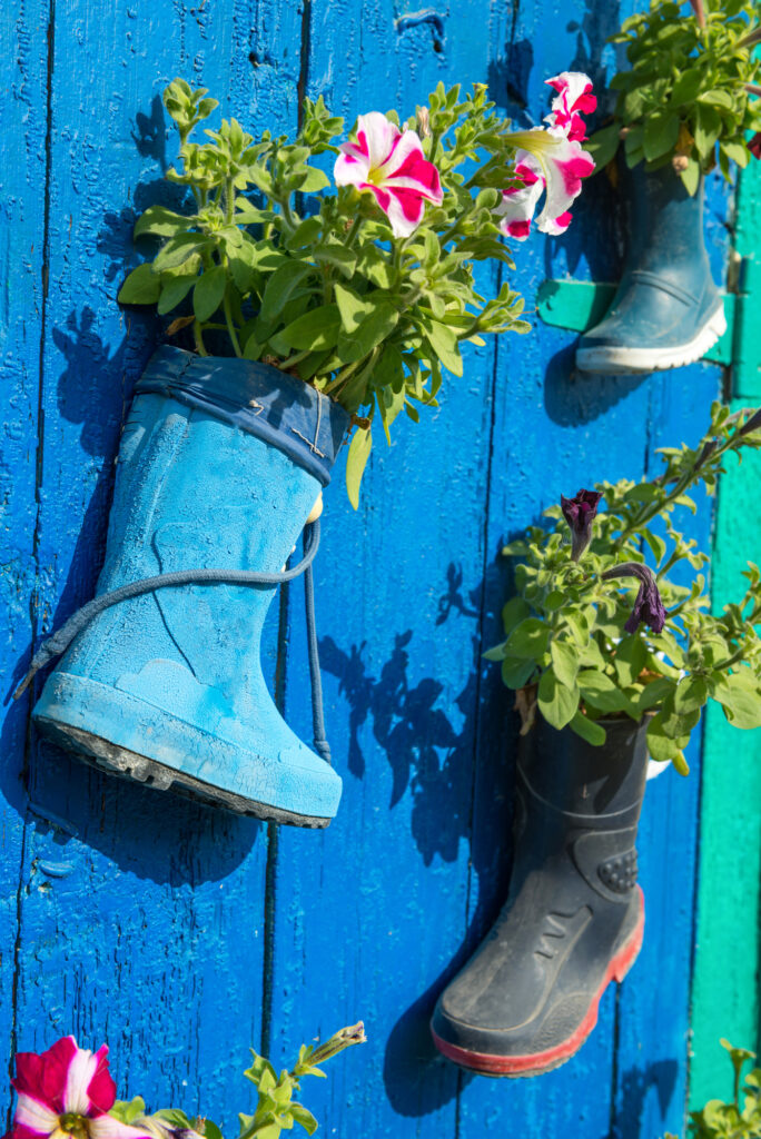 Old children rubber boots with blooming summer flowers on the entrance door of a house