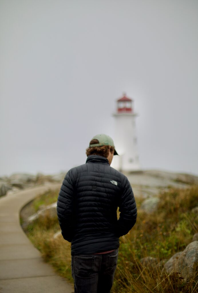 man wearing north face jacket walking near a lighthouse